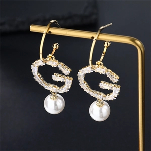 Elegant gold bow earrings with crystal letter G and white pearl on a display stand