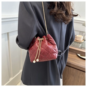 Detail of red quilted bucket bag with gold chain strap and pearl accents on model