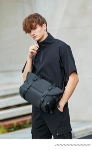 Man wearing black tactical messenger bag with adjustable buckles in a modern urban street setting