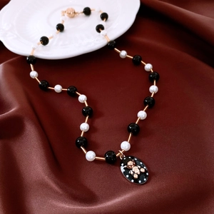 Detail of beaded necklace with gold tubes, black enamel pendant and small gold bear