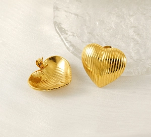 Macro detail of gold heart-shaped earrings with vertical ripples and butterfly backing