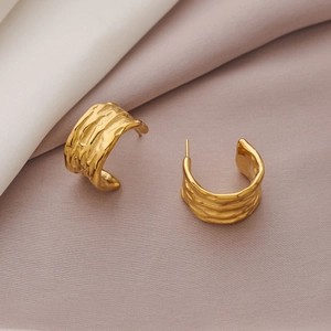 Macro detail of golden hammered texture C-shape stainless steel earrings on soft silk cloth