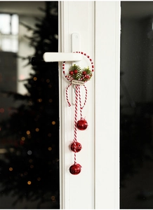 Close-up of red metal bells with pine needles and berries hanging on a white door