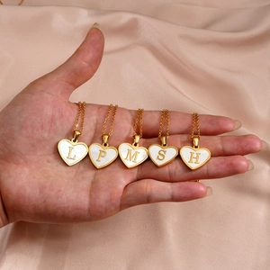 Close-up of gold heart necklaces with white shell inlay and letters on pink silk