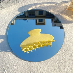Détail d'une pince à cheveux jaune en acétate avec texture marbrée sur un miroir