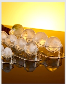 Close-up of a transparent sphere ice mold tray with clear round ice balls on a dark surface