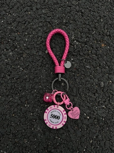 Macro view of rose red braided keychain with poker chip and heart pendant on ground