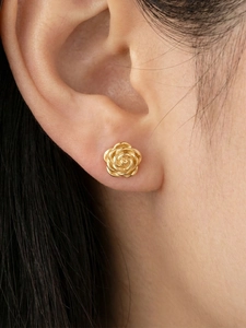 Close-up of golden 3D rose earrings on model's ear showing detailed petal textures