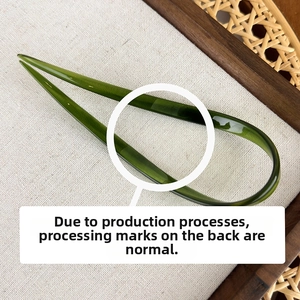 Close-up of translucent dark green U-shaped hair pin on natural linen background