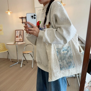 Detail of white lace tote bag with blue floral pocket shown in a mirror selfie