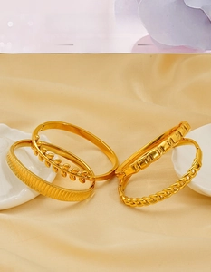 Gros plan détaillé de quatre bracelets en acier inoxydable doré texturé sur tissu en soie