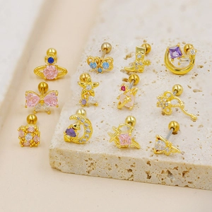 Golden planet and bow piercing studs with colorful zircon crystals on stone surface