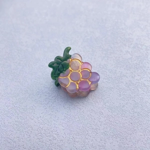 Detail of purple grape hair clip made of translucent resin with gold trim and green leaf