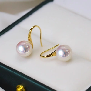 Elegant gold hook earrings with round white pearls featuring a pinkish luster on a green box