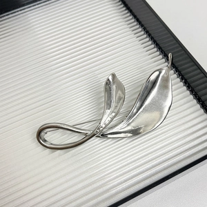 Macro detail of silver tulip leaf brooch with polished metallic finish and modern art design