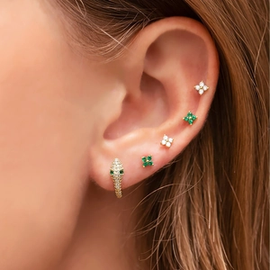 Detailed close-up of zircon snake hoop and blue flower stud earrings on ear model
