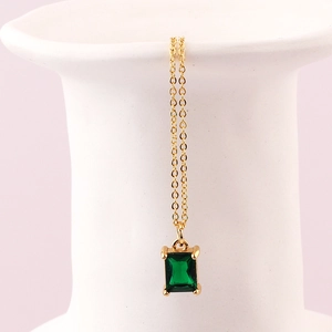 Dettaglio di una collana con ciondolo smeraldo verde appesa a un vaso di ceramica bianca