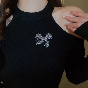 Detail of bow-shaped brooch with purple and green crystals on black knitwear