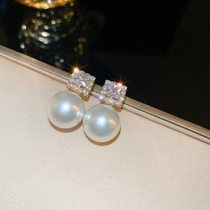 Macro detail of elegant gold-plated stud earrings with square zircon and white pearl