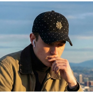 Detail of black polka dot baseball cap with gold embroidery worn by model at sunset