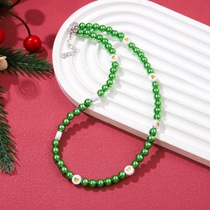 Christmas necklace with green beads and gold hearts on white ripple plate with red background