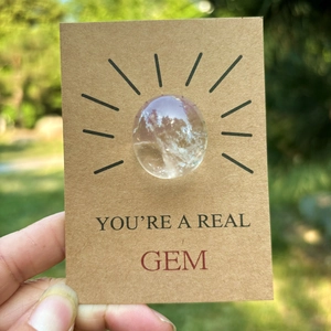 Healing crystal on 'You're a Real Gem' card held outdoors with natural sunlight