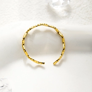 Detailed top view of a gold open ring with leaf pattern on a white surface with ice