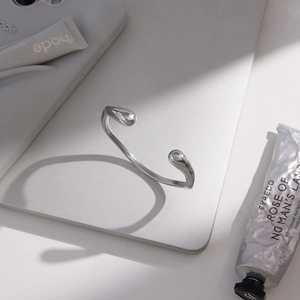 Artistic top view of minimalist silver irregular open bangle with bean-shaped ends