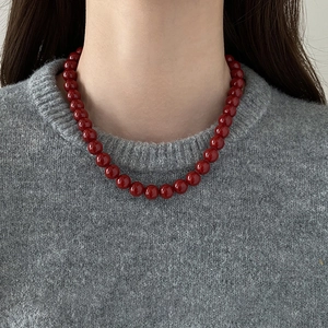 Gros plan d'un collier de perles en verre rouge foncé sur un pull gris chic