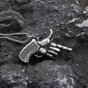 Detailed view of silver pistol gesture pendant on a textured dark volcanic stone background