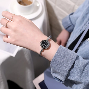 Detail of silver mesh bracelet watch with black quartz dial worn in a cafe setting