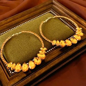 Detail view of gold hoop earrings with amber teardrop gems on green velvet