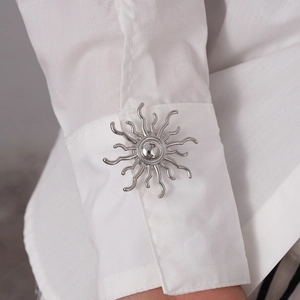 Macro shot of a silver sunburst metal brooch pinned on a white shirt cuff