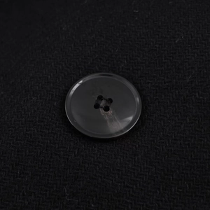 Detail of four-hole black button on textured herringbone coat fabric with waist belt