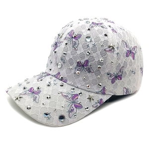 Detail einer weißen Spitzen-Basecap mit lila Schmetterlingen und funkelnden Strasssteinen