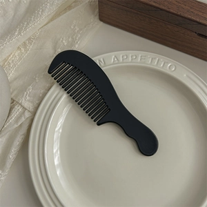 Detail of a large black acetate wide-tooth hair comb placed on a vintage plate