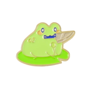 Detailed view of enamel frog pin with utility knife on green lily pad with gold edges