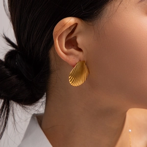 Macro shot of matte gold scallop shell earrings with radiating texture on a female model