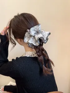Détail d'un grand chouchou en dentelle à fleurs noir et blanc sur des cheveux tressés