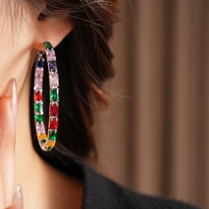 Close-up of luxury silver hoop earrings with colorful rectangular zircon stones on model
