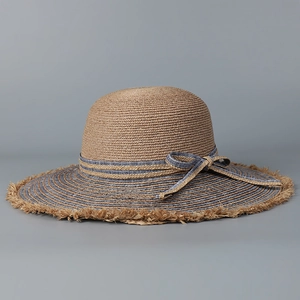 Detail of raffia sun hat with blue striped ribbon bow and raw frayed edges for summer