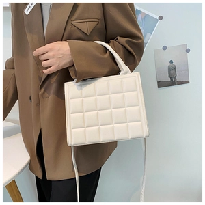 Detail of white quilted square handbag with textured pattern and crossbody strap