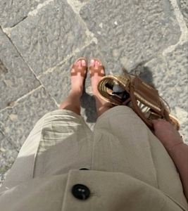 POV shot of brown leather H-cut sandals paired with beige linen shorts and a straw tote bag