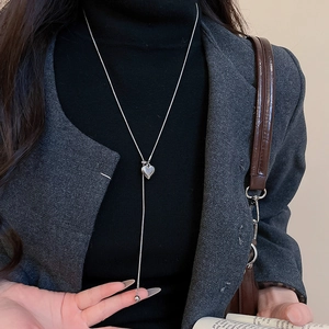 Close-up of silver Y-shaped pearl heart pendant necklace styled over a black sweater