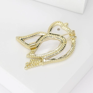 Elegant gold-tone dove brooch with openwork design and beaded edges on white block