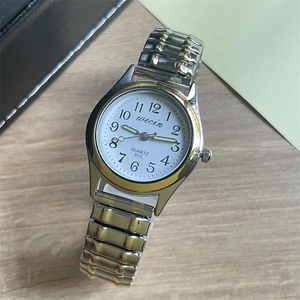 Detail of silver and gold tone quartz watch with elastic steel strap on a wooden desk