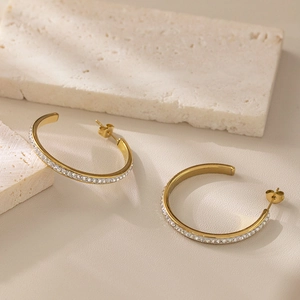 Elegant gold C-shaped hoop earrings with shimmering zircons on stone background