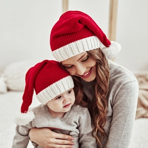Close-up of mother and baby wearing red knitted Christmas hats with white pom poms
