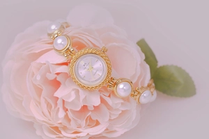 Detail of luxury gold watch with pearl strap displayed on a pink flower petal