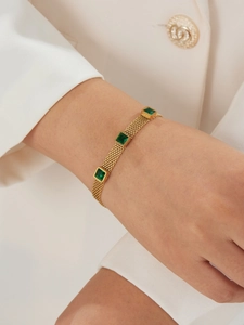 Detail view of gold mesh chain bracelet with three square emerald green zircons
